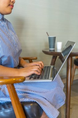 İş kadını koltukta oturuyor ve kahve dükkanında dizüstü bilgisayar yazıyor.