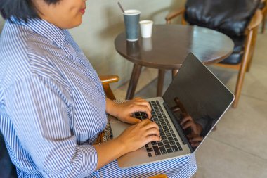 Asyalı serbest çalışan kadın kahve masasında oturuyor ve dizüstü bilgisayar yazıyor. 