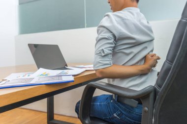 Ofis çalışanı dizüstü bilgisayarın önünde otururken sırt ağrısı çekiyor.