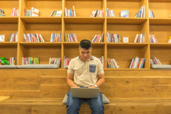 Estudante asiático usando laptop no fundo de estante de biblioteca de madeira — Fotografia de Stock