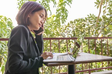 Siyah takım elbiseli kadın cep telefonu ve laptop kullanıyor. 