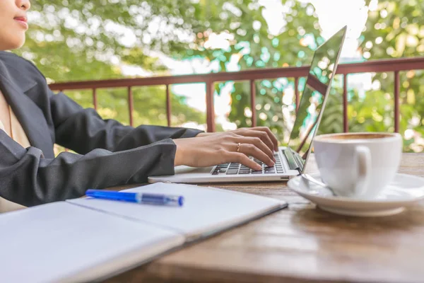 Woman in black suit typing laptop outdoor garden view