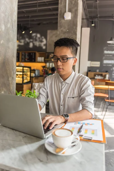 Νεαρός Ασιάτης ελεύθερος επαγγελματίας που εργάζεται σε φορητό υπολογιστή στο καφέ — Φωτογραφία Αρχείου