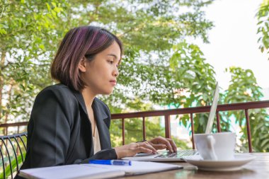 Siyah takım elbiseli bir kadın bir fincan kahvenin yanında dizüstü bilgisayar yazıyor.