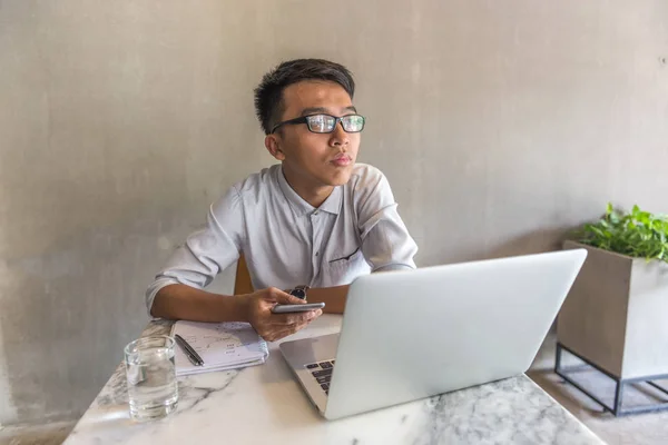 Hombre joven usando el teléfono celular y el portátil y pensando en la oficina — Foto de Stock