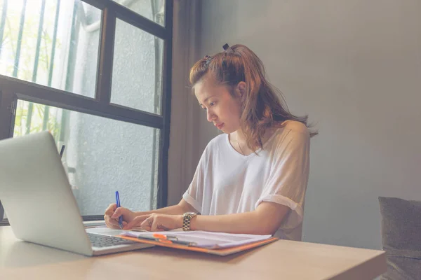 Mujer asiática caligrafía al lado de portátil y ventana — Foto de Stock