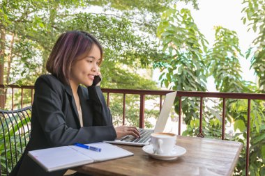 Dışarıda bahçe manzarasında dizüstü bilgisayarda çalışan genç bir kadın.