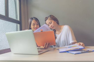Bilgisayarın yanındaki belgelerde çalışan iki genç bayan.