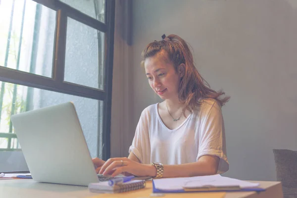 Joven dama feliz en camiseta blanca usando el ordenador portátil mientras trabaja — Foto de Stock