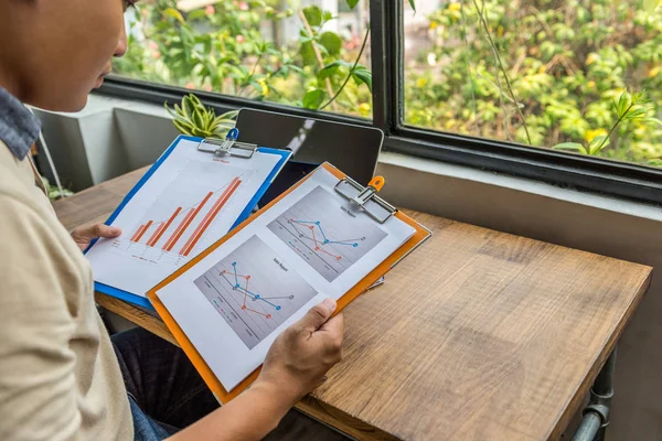 Asian freelancer holding and analyzing statistic documents at rustic workplace