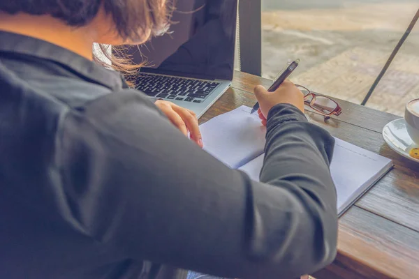 Bakifrån av kvinna skriva anteckningsbok bredvid bärbar dator — Stockfoto