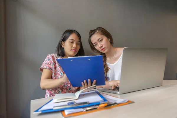 Две офисные дамы, работающие на ноутбуке и читающие отчет — стоковое фото