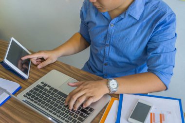 Genç adam dizüstü bilgisayar ve tablet üzerinde çalışıyor.