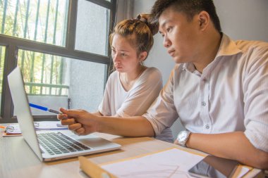 Pencerenin yanında dizüstü bilgisayarla çalışan genç çift. 