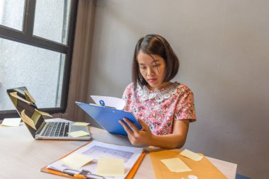 Pencerenin yanında dizüstü bilgisayarla çalışan genç bir kız.