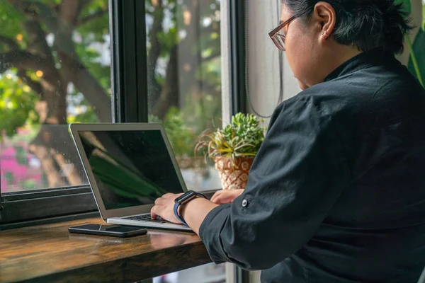 Asian millennial woman working on laptop next to green plant