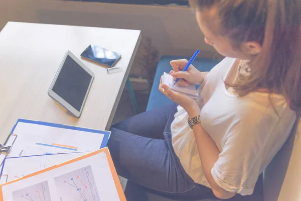 Young woman handwriting into notes in office