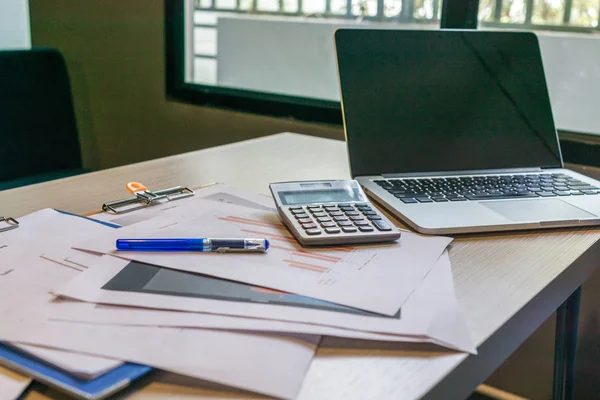 Unorganized messy desk with laptop , calculator and documents at workplace