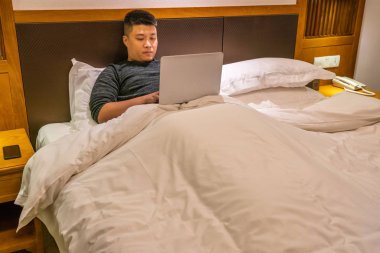 Yatakta yatarken ve dizüstü bilgisayar kullanarak genç adam