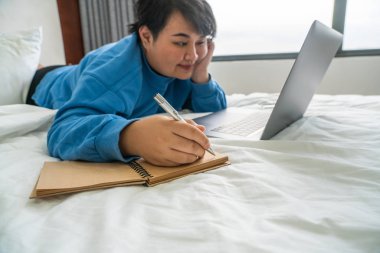 Gülümseyen kadın not yazıyor ve laptop kullanıyor.