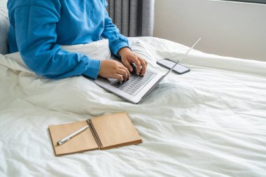 Beyaz bir yatakta dizüstü bilgisayar kullanan kadınlar.