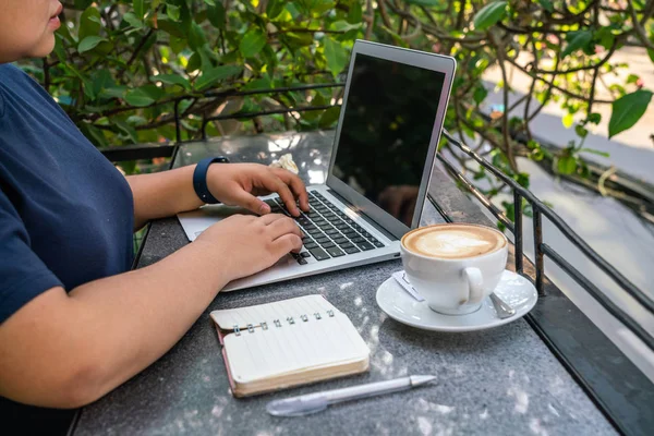 Freelancer pomocí notebooku vedle notebooku a šálek cappuccino — Stock fotografie