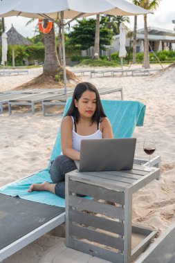 Genç Asyalı serbest yazar sahilde dizüstü bilgisayarla çalışıyor.