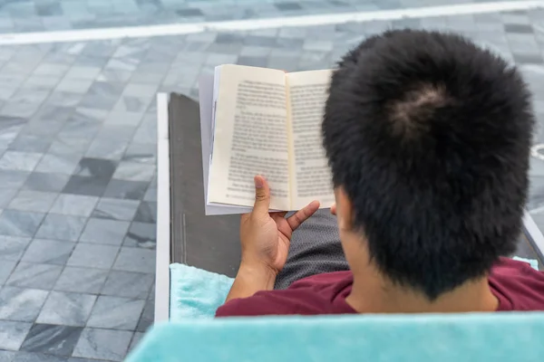 Asian man relax and reading book in swimming pool