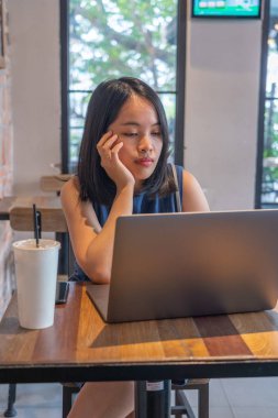 Kahve masasında dizüstü bilgisayarda çalışan Asyalı evli kadın.