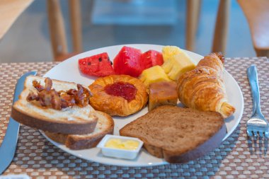 Ekmek dilimleri, meyveler, kruvasan, tereyağı ve çilek reçeli ile kahvaltı