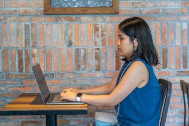 Asya milenyumu, kırsal kafeteryadaki ahşap masada dizüstü bilgisayar kullanıyor.