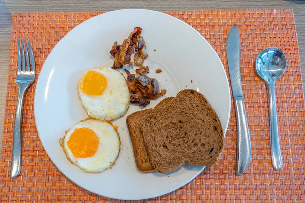 Assiette d'œufs ensoleillés avec jambon et pain brun — Photo