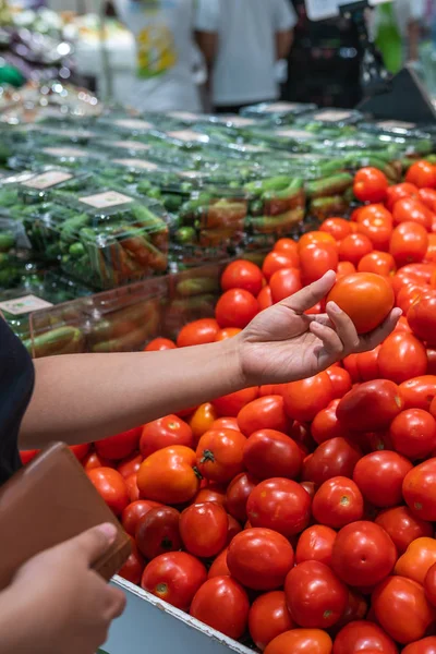 Женщина держит сумочку и собирает идеальные помидоры в продуктовом магазине — стоковое фото