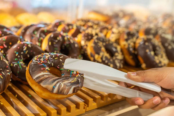 Menselijke hand met behulp van klem plukken chocolade donut in banketbakkerij — Stockfoto