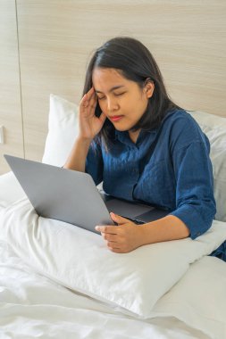 Yatakta dizüstü bilgisayarla çalışan genç bir kadın baş ağrısı hissediyor 