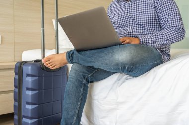 Otel odasında bavulun yanında dizüstü bilgisayar kullanan bir iş adamı.
