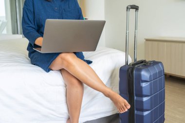 İş gezisinde bavulun yanında dizüstü bilgisayar kullanan bir kadın.