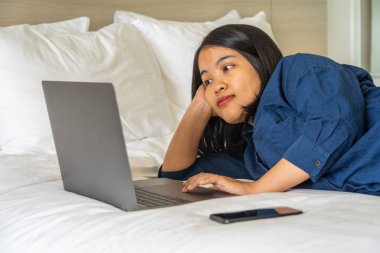 Genç bir kadın yatağında dizüstü bilgisayar kullanıyor.