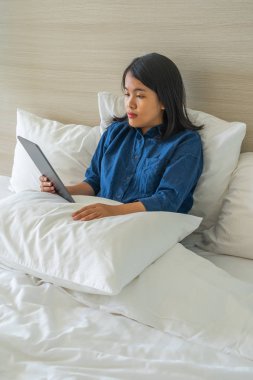 Yatak odasında dijital tablet kullanan Asyalı kadın