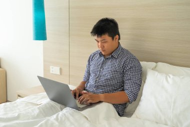 Yatak odasında lambanın yanındaki bilgisayarı kullanan genç adam.