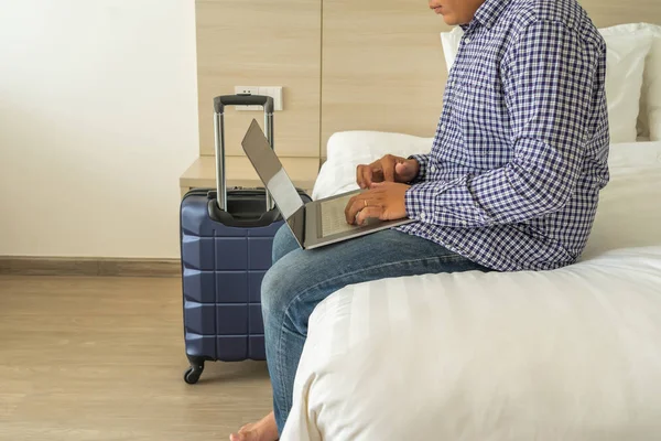 İş adamı iş gezisinde bavulun yanında dizüstü bilgisayar kullanıyor.