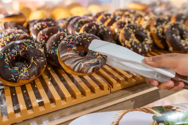 Menselijke hand met behulp van klem plukken bevroren chocolade donut bij de bakkerij — Stockfoto