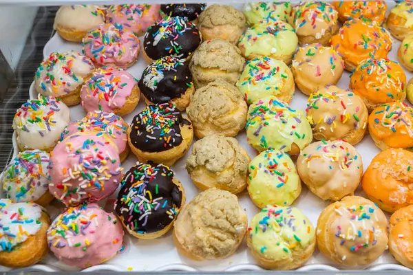 Beberapa kue puff manis berwarna dengan topping cokelat beku di bakeshop — Stok Foto