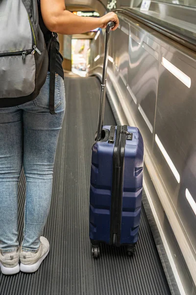 Nuori nainen, jolla on kädessään matkalaukku liukuportaissa lentokentällä — kuvapankkivalokuva