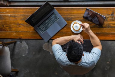 Asian freelancer working with laptop and enjoying hot cappuccino