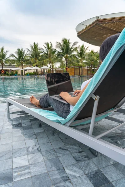 Mulher asiática usando laptop em um banco na piscina — Fotografia de Stock