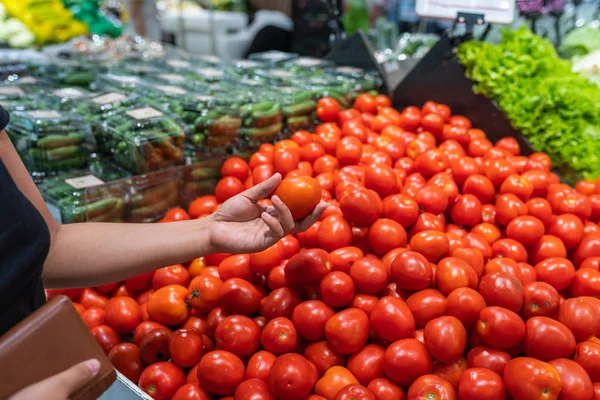 Женщина держит сумочку и покупает помидоры в продуктовом магазине — стоковое фото