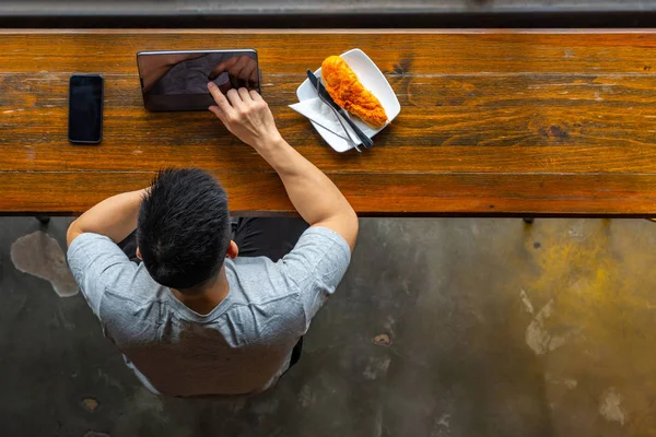Top view of Asian millennial using tablet while having breakfast