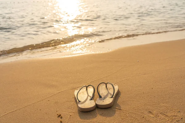 Paar Pantoffeln am ruhigen Strand im Sonnenuntergang — Stockfoto