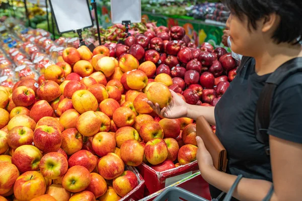 Молодая азиатка покупает яблоко в фруктовом киоске в супермаркете — стоковое фото